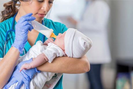 Young female nurse feeds formula to an infant baby with a bottle.