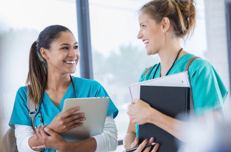 Two pretty young female diverse nursing students sharing nursing school tips