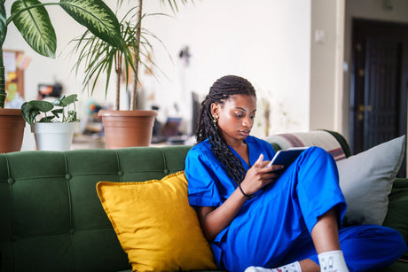 Female nursing student in scrubs on her couch with an ipad