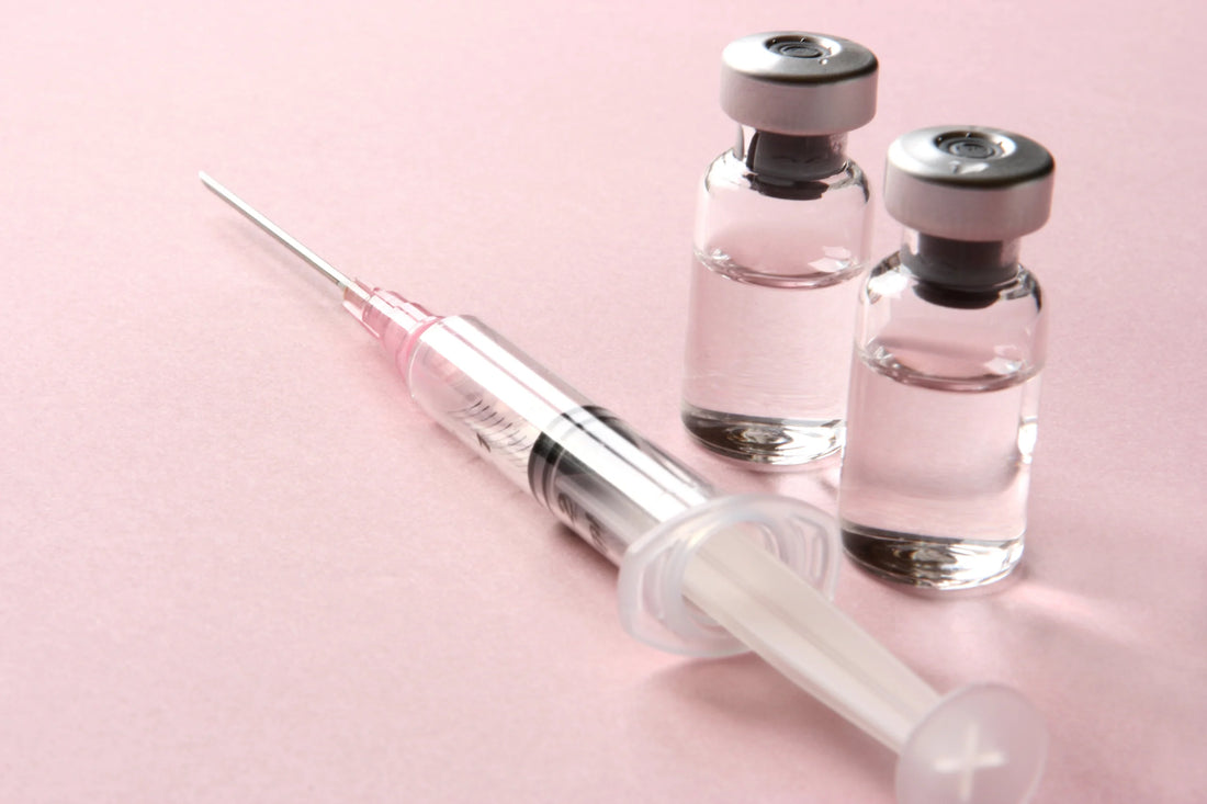 Syringe on a pink background with 2 vials of medication