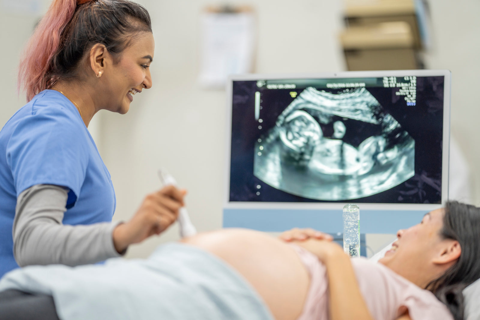Young female nurse does a sonogram on the belly abdomen of a supine pregnant woman.