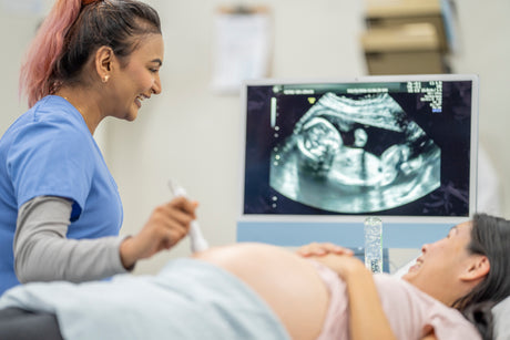 Young female nurse does a sonogram on the belly abdomen of a supine pregnant woman.
