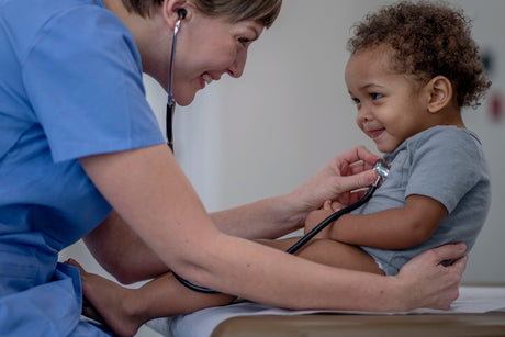 Pediatric nurse with stethoscope against little boy's chest