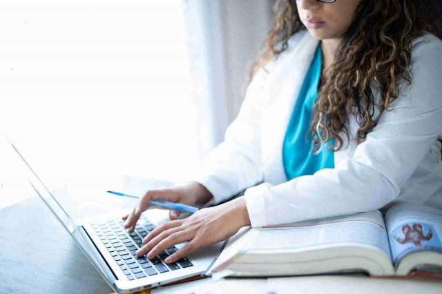 Female nursing student in scrubs and a white lab coat studies for the nclex