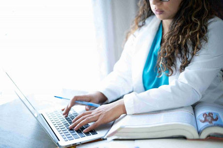 Female nursing student in scrubs and a white lab coat studies for the nclex