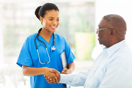 Young African American pretty female nurse shakes hands with a sitting senior black man.