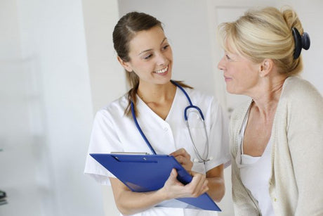 Young nurse consults an older blond woman while taking notes on a chart nurse speaking to patient