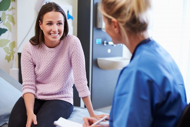 A young blond nurse in blue scrubs consults a pretty young brunette woman for presumptive signs of pregnancy
