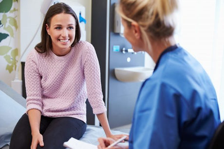 A young blond nurse in blue scrubs consults a pretty young brunette woman for presumptive signs of pregnancy