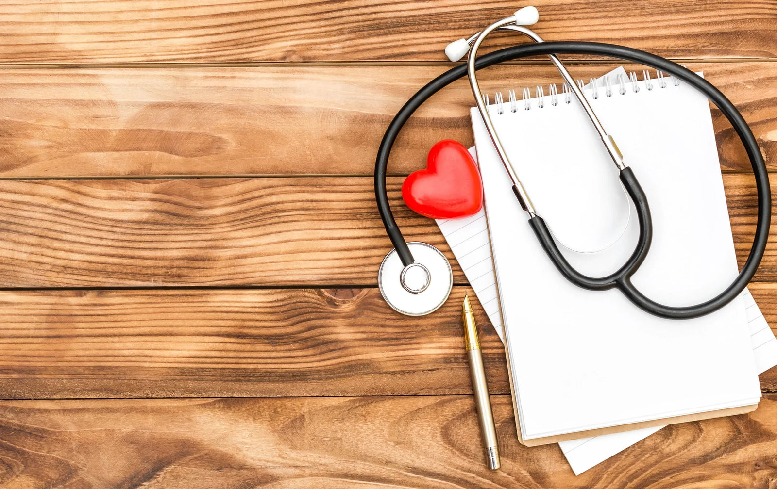 Stethescope and red heart on top of head to toe assessment with wood background