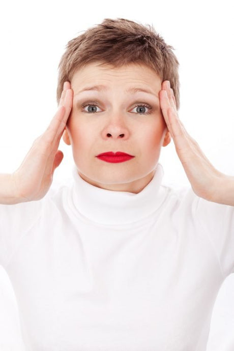 White woman in white holding her temples suffering from Increased Intracranial Pressure
