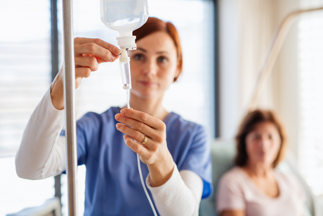 Female woman nurse holding IV bag and observing drip factor for a woman patient in a hospital bed