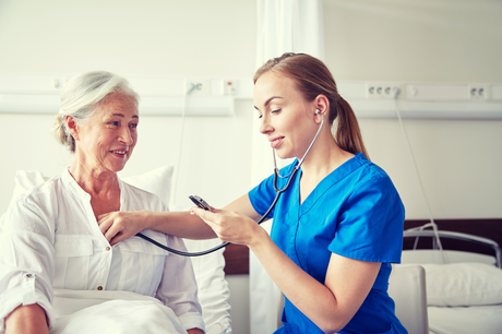 Young pretty blond female nursing student checking cardiac output on an older woman patient in a hospital