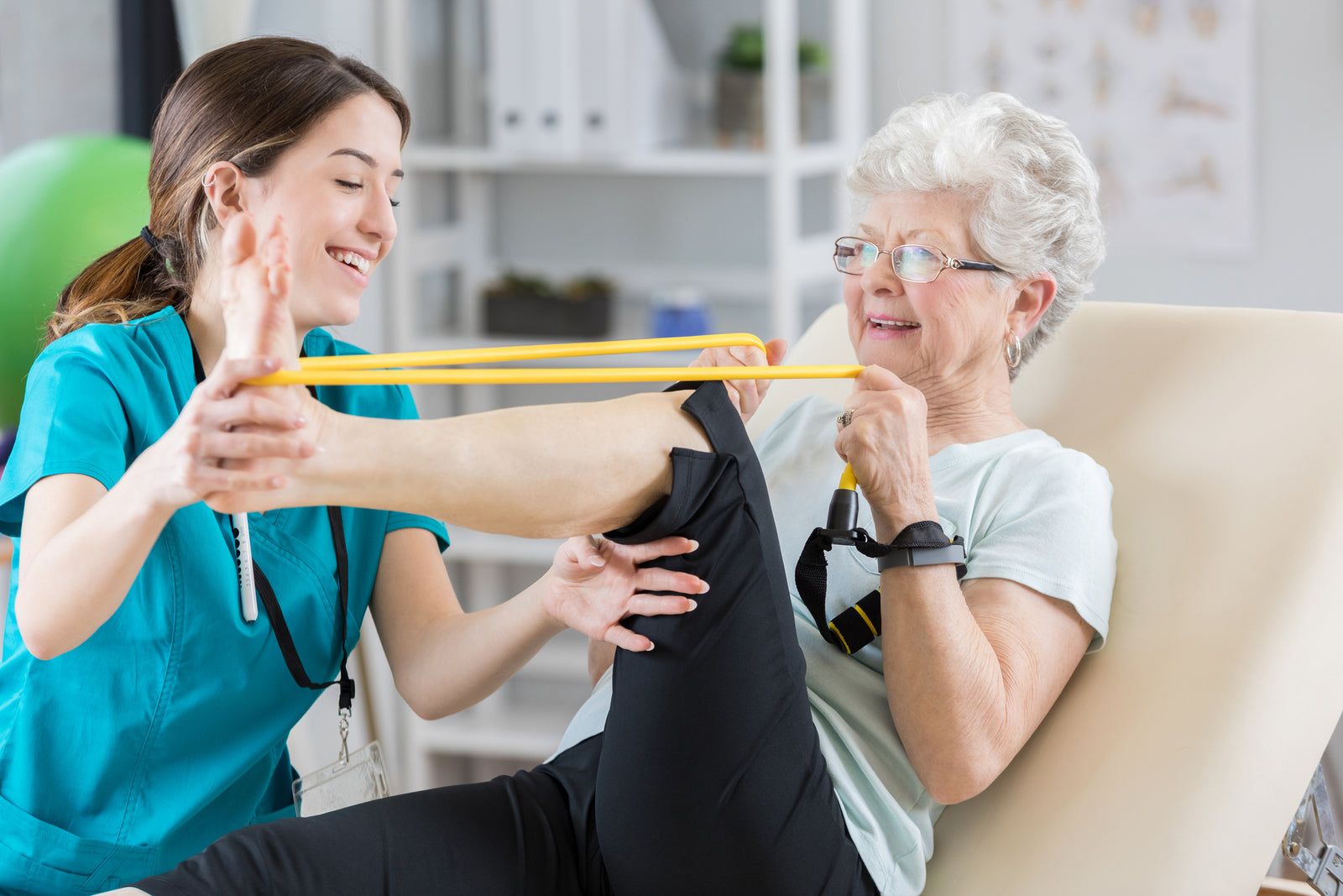 A young woman female nurse helps a older elder woman with her foot flexion and extension exercises.