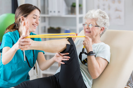 A young woman female nurse helps a older elder woman with her foot flexion and extension exercises.