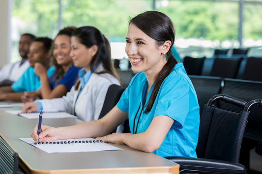A cheerful young nursing student sits in a classroom during a medical training lecture and takes notes.