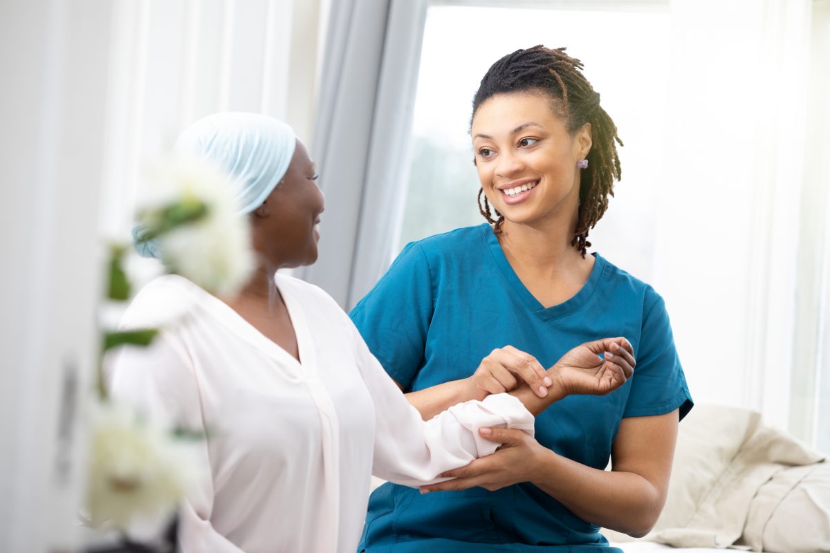Black young nurse checks the pulse of an African American female patient.