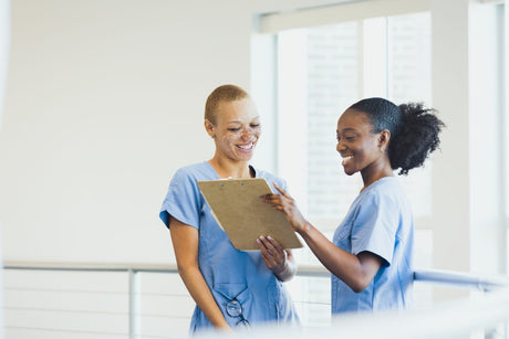 Two female nurses smile as they review patient records