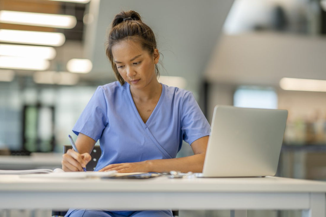 A woman wearing scrubs diligently studies at a desk in a modern educational building. Nursing student studying