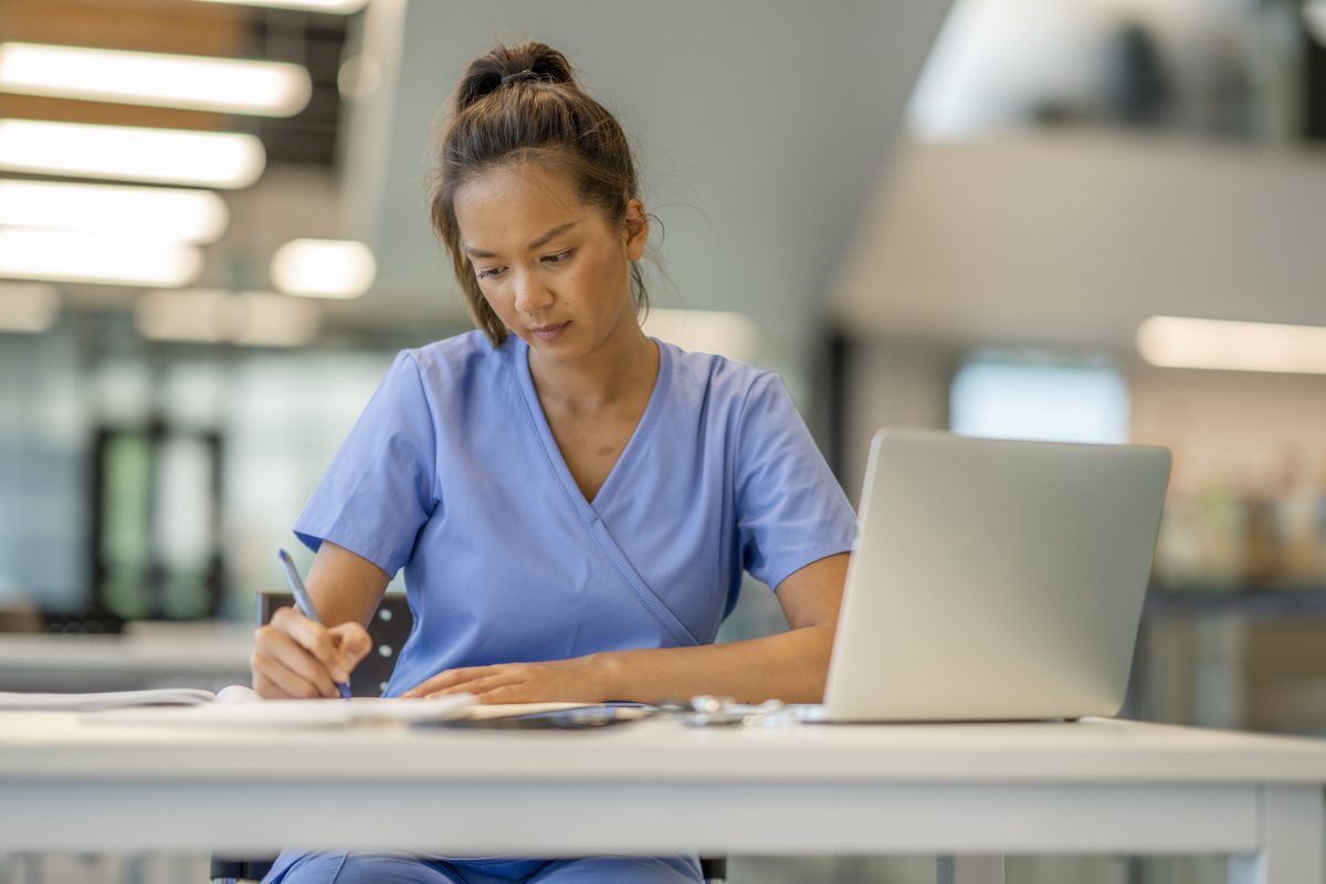 A woman wearing scrubs diligently studies at a desk in a modern educational building. Nursing student studying
