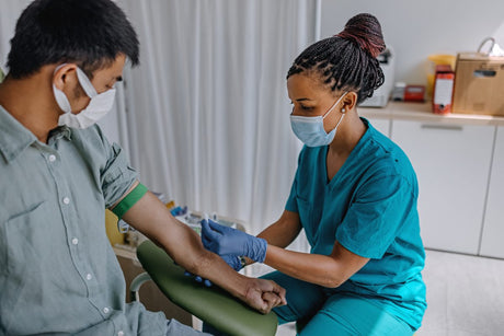 African American Black female nurse in a mask drawing blood from a masked man .How to Become a Phlebotomist + Salary Expectations