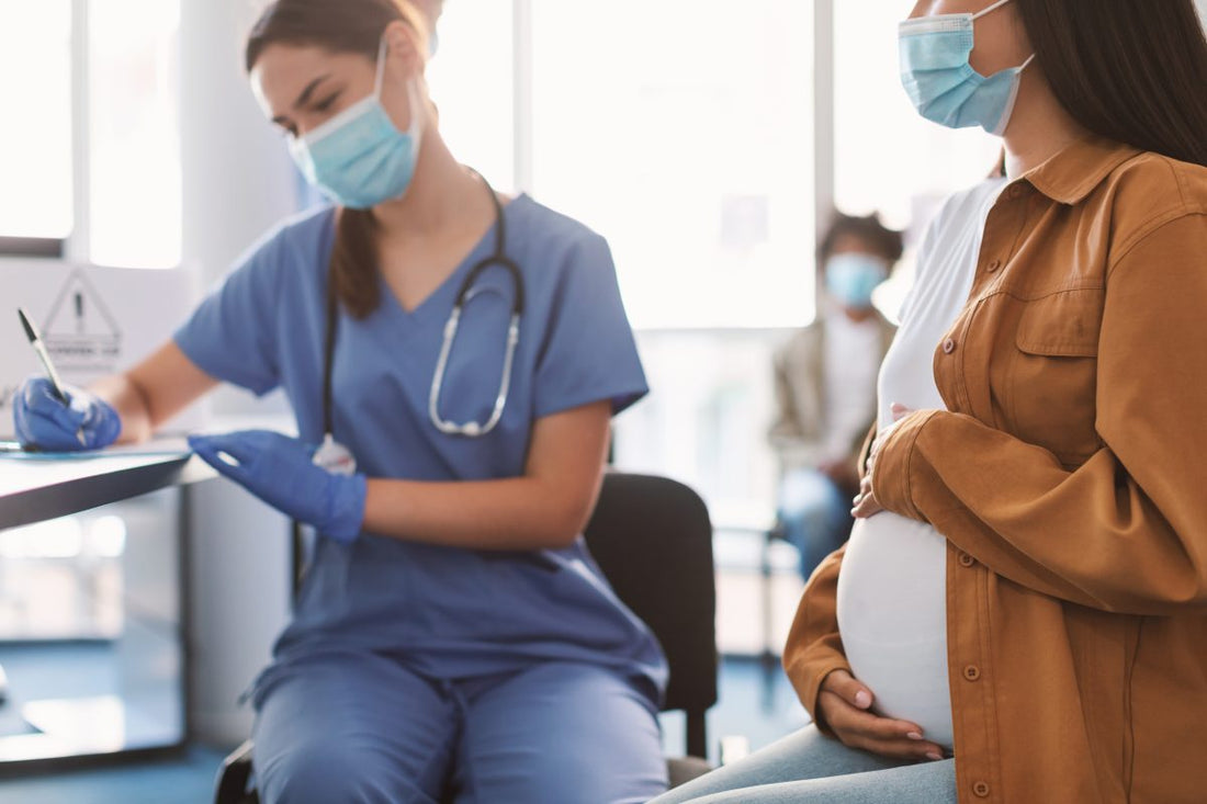 Pregnant woman in face mask visit nurse gynecologist at hospital or medical clinic for consultation, doctor filling health record, selective focus on belly. Mother healthcare check up. Gynecology concept.