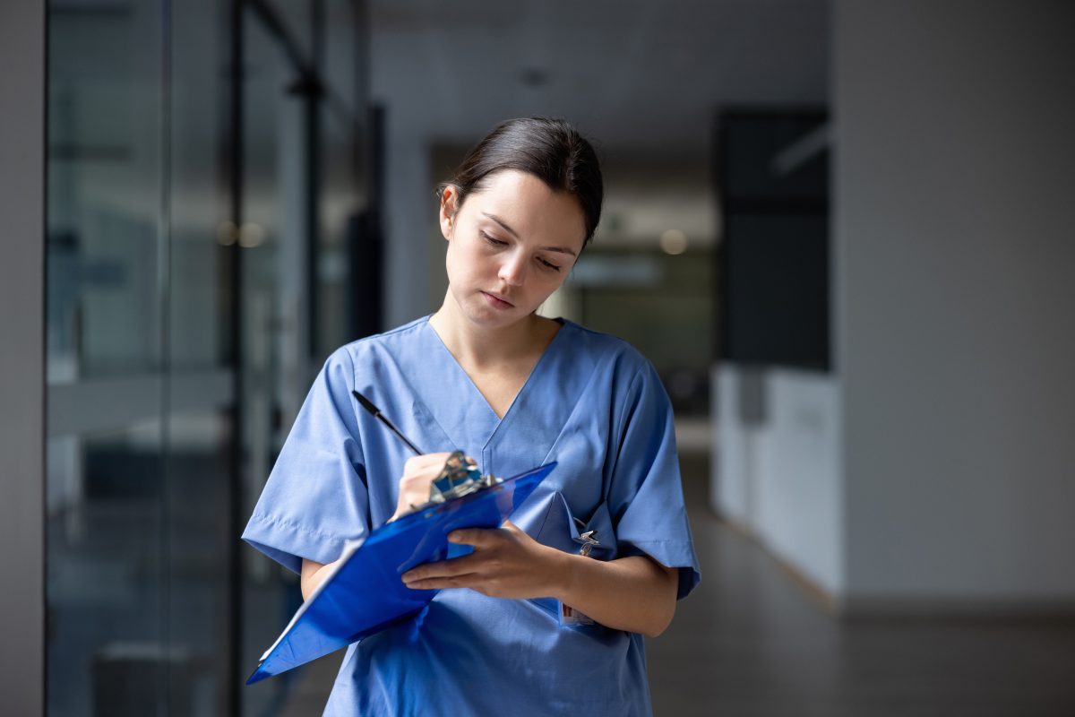 Latin American female nurse working at the hospital writing on a clipboard in the corridor - healthcare workers concepts. Nurse working at the hospital writing on a clipboard.