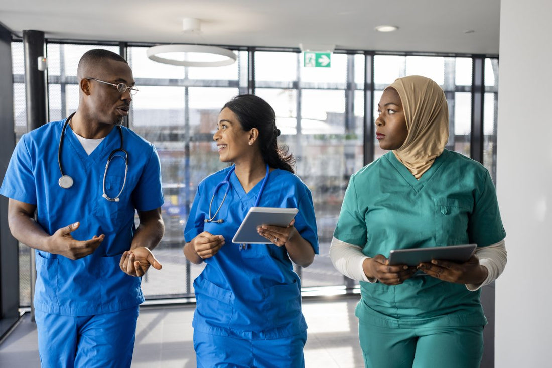 Mixed ethnic group of medical nursing nurse professionals walking down a corridor together in the North East of England. They are working a shift at a hospital and are dressed in scrubs. The women are carrying/using digital tablets.