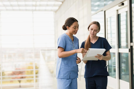 Standing on a walkway inthe hospital atrium area, two female nurses discuss the schedule for the day.
