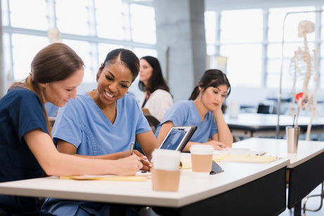 Two mid adult female nursing students use an x-ray displayed on a digital table to work together on their homework.