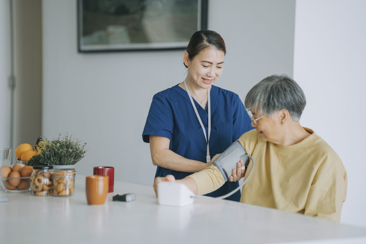 A young Asian nurse in scrubs administers a blood pressure test with a BP cuff on an elder woman. Stable vs Unstable Angina: an Acute Coronary Syndrome Overview