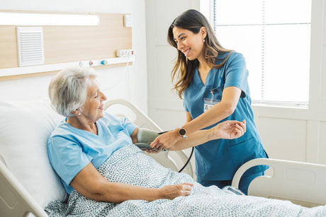 Nurse talking to senior woman in hospital bed. She is measuring her blood pressure. Senior woman in hospital bed