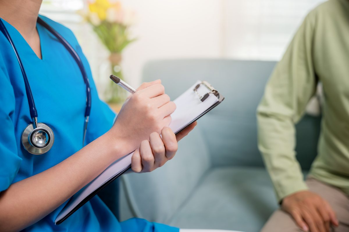 Asian young nurse writing prescription during home visit sick elder old man