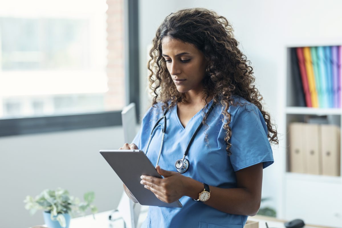 Female nurse using her digital tablet while standing in the consultation.