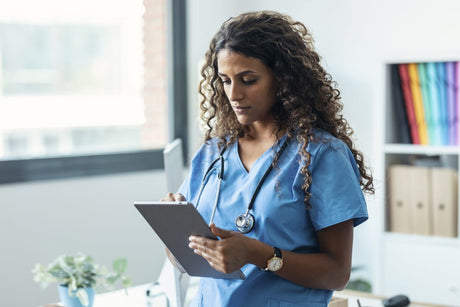 Female nurse using her digital tablet while standing in the consultation.
