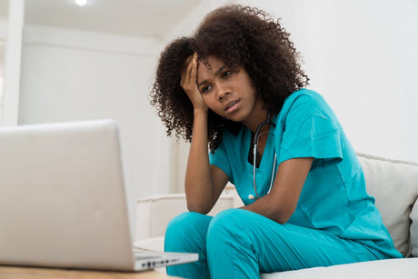 Stressed African American Black female doctor with hand on forehead while working with laptop computer in hospital. Unhappy female nurse in office at hospital