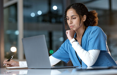 Female Nurse, thinking and writing with laptop at night for healthcare solution, idea or planning at hospital. Woman medical nurse working late in focus for research with notebook and computer at clinic