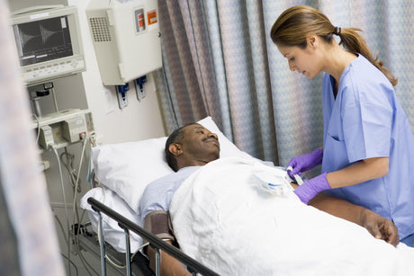 Female Nurse Caring For Patient In Hospital Bed Looking Down