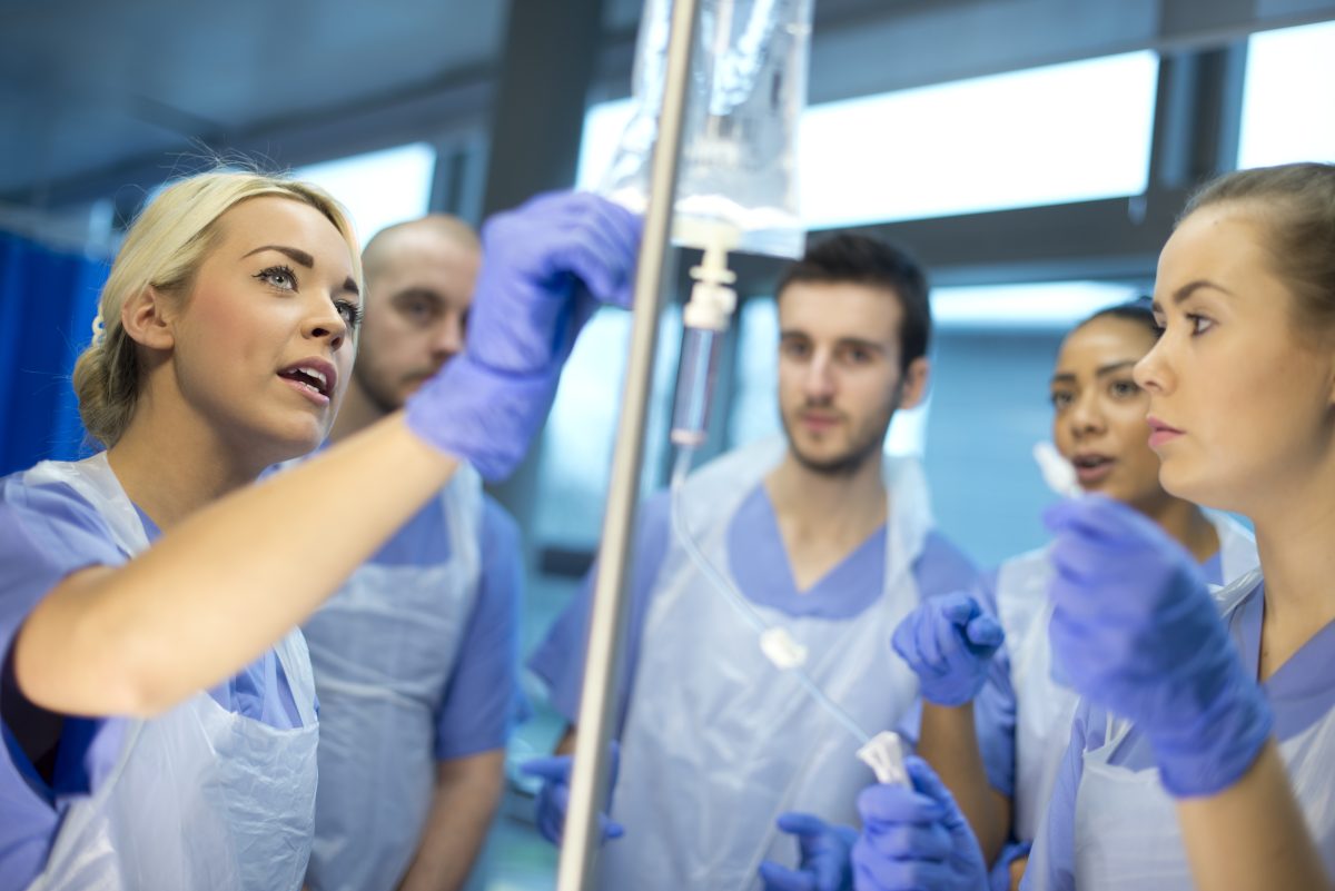nurse shows other nurse trainees how to use the IV drip during a nursing class.