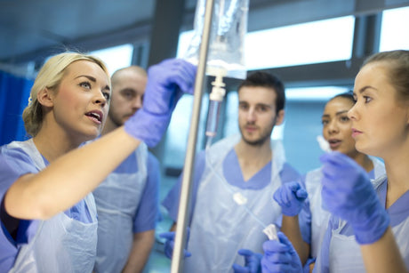 nurse shows other nurse trainees how to use the IV drip during a nursing class.