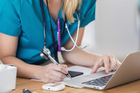 Medical professional uses laptop at hospital. Unrecognizable Caucasian nurse writes something while using a computer in a doctor's office or hospital.