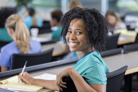 Smiling African American Black nursing student taking nursing notes on a yellow pad in a class on nursing.