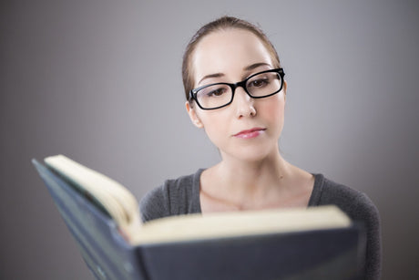 Studious serious nursing student in reading glasses studies a nursing textbook
