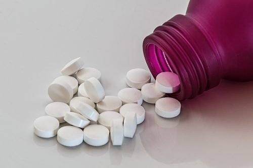 White pills poured out of a purple bottle.